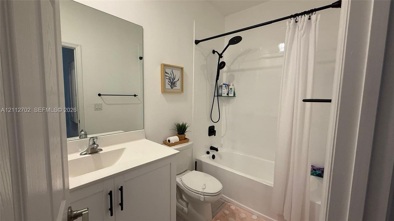 Bathroom featuring a white vanity cabinet with a solid-surface countertop, full-width mirror, and matte black hardware including a showerhead assembly and towel bar