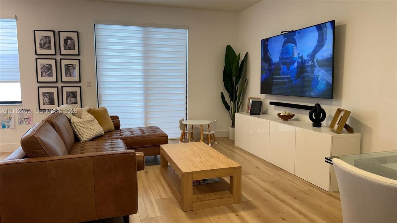 Living area featuring wood-finish flooring, dual-layered light-filtering window treatments, and high-gloss white built-in cabinetry