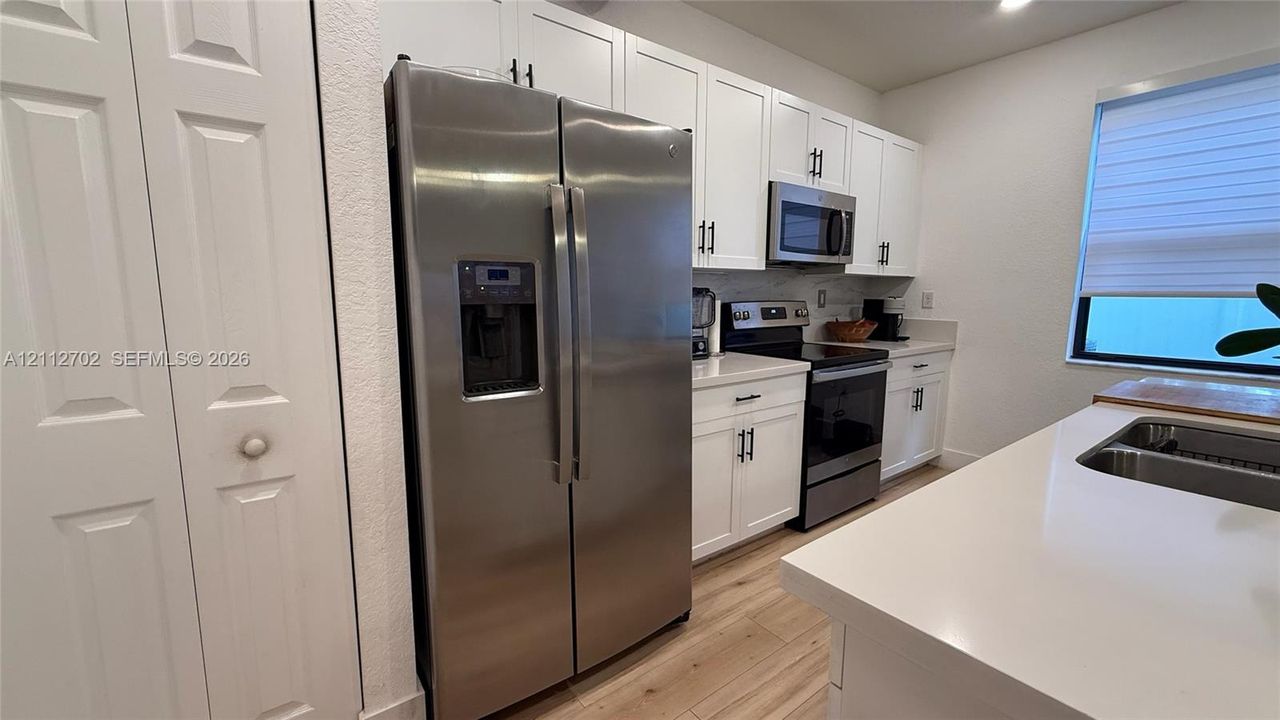 Kitchen featuring white shaker-style cabinetry, stainless steel appliances, solid surface countertops, a stainless steel undermount sink, and wood-finish flooring