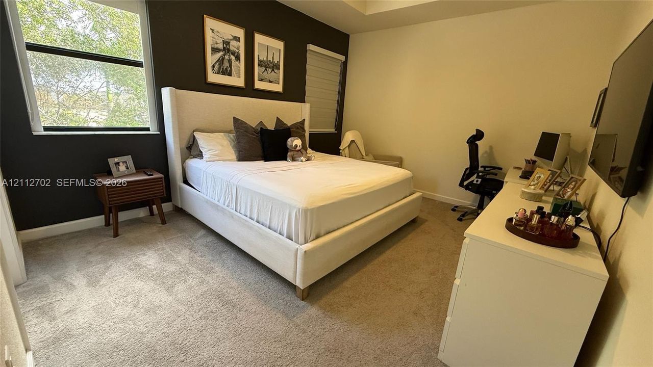 Bedroom featuring a tray ceiling, neutral wall-to-wall carpeting, and a dark-toned accent wall