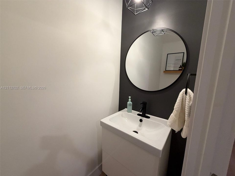 Wall-mounted vanity with integrated sink, matte black single-handle faucet, circular wall mirror, and geometric pendant lighting