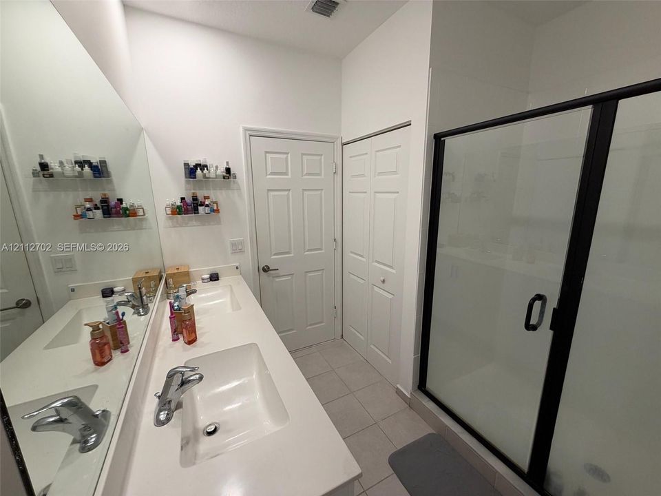 Dual vanity with rectangular drop-in sinks, expansive wall-mounted mirror, ceramic tile flooring, and walk-in shower featuring a black-framed glass enclosure