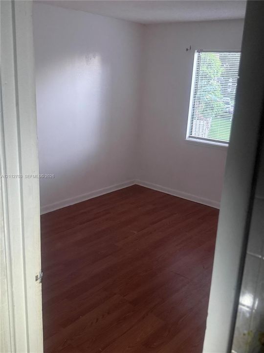 Interior space featuring wood-finish flooring, white walls, and a window with horizontal blinds
