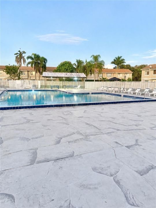 Swimming pool featuring a stone-patterned concrete deck, a covered pavilion, and surrounding perimeter fencing