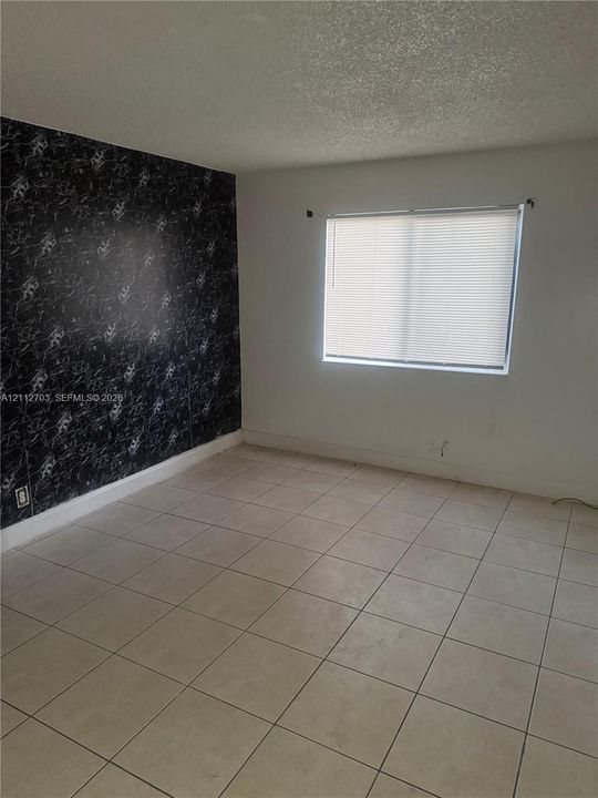 Room featuring large-format ceramic tile flooring, a black-and-white patterned accent wall, and a horizontal window with integrated blinds
