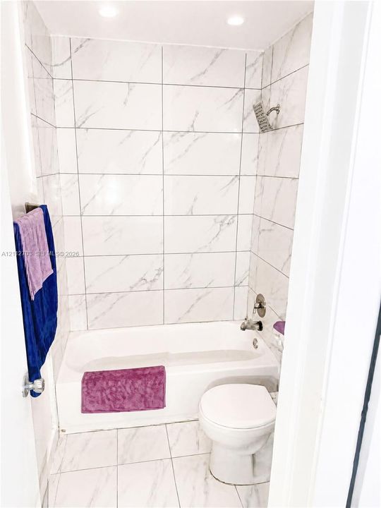 Full-height stone-finish tile surround, integrated soaking tub, recessed ceiling lighting, and large-format tile flooring