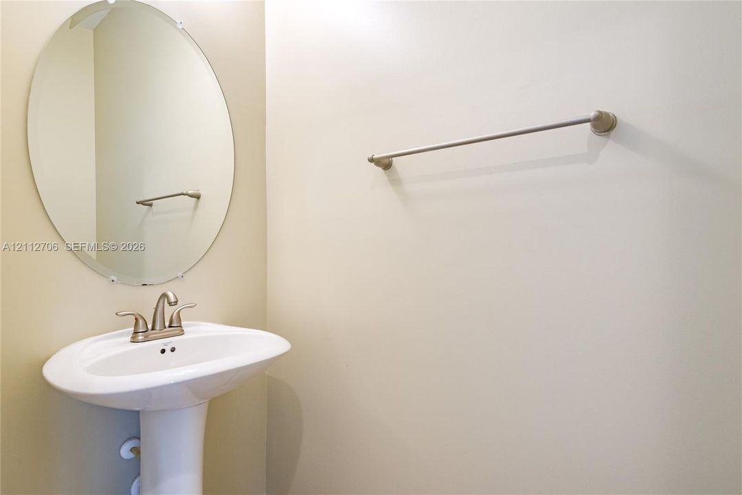 Oval wall-mounted mirror featuring a polished metal finish, white pedestal sink, and metallic faucet fixture with dual handles