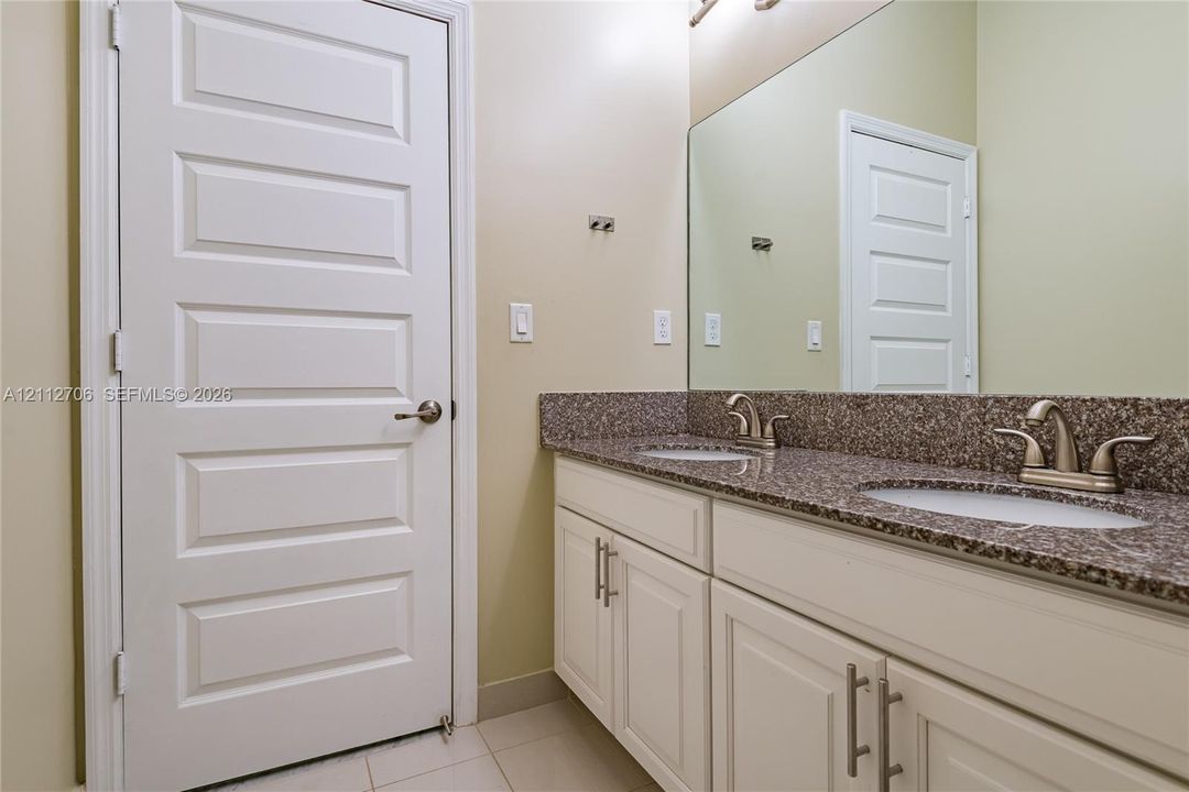 Dual-sink vanity featuring stone-finish countertops, white cabinetry with brushed-metal pulls, and a large-format vanity mirror