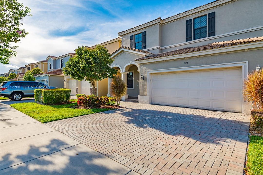Two-story stucco exterior featuring a tiled roof, paver driveway, arched entryway, and multi-pane windows with decorative shutters
