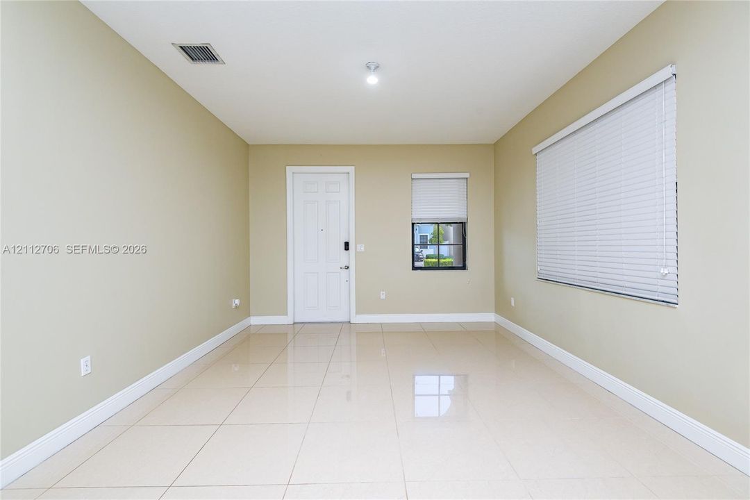 Neutral-toned interior featuring large-format tile flooring, six-panel entry door, and horizontal window blinds