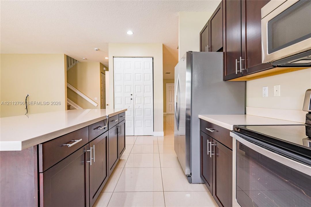 Kitchen featuring dark wood cabinetry, solid-surface countertops, tile flooring, and stainless steel appliances