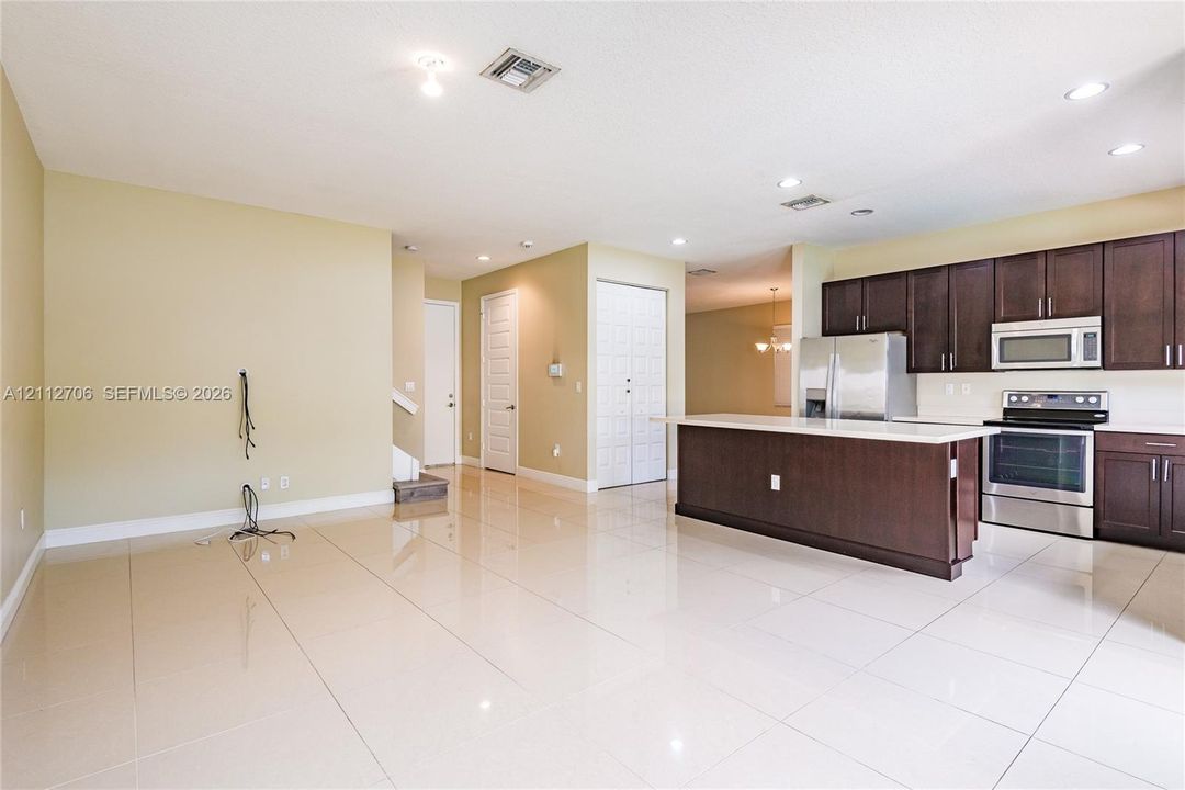 Open-concept kitchen featuring dark wood cabinetry, an island with a quartz countertop, stainless steel appliances, and large-format tile flooring throughout