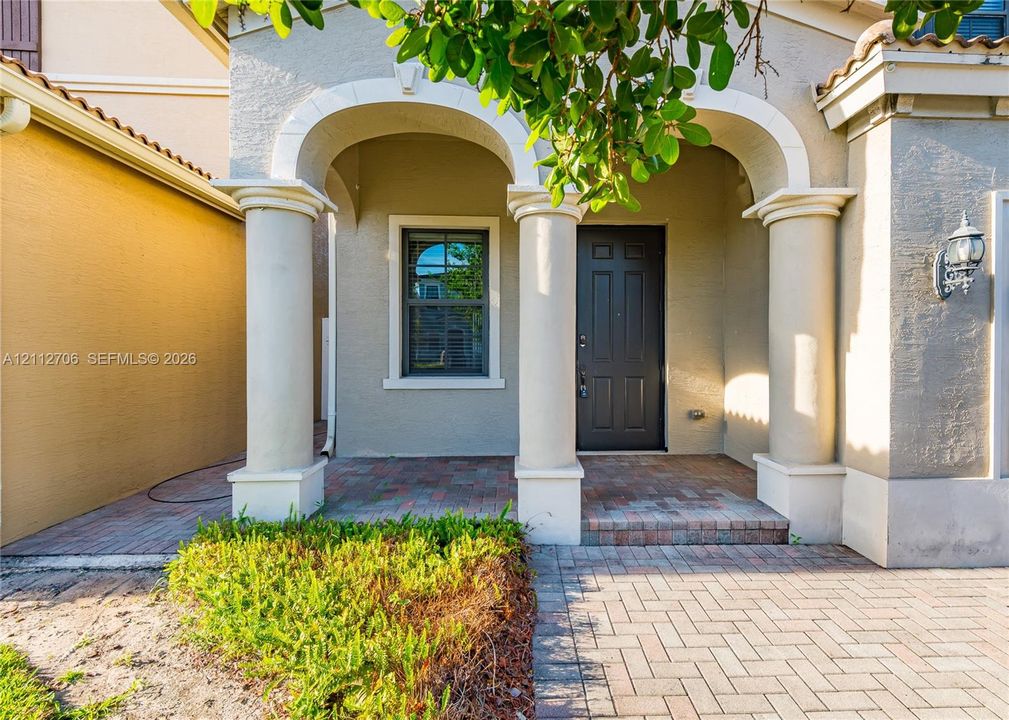 Covered entryway featuring structural columns with arched masonry detailing, a paver stone porch, and a multi-panel front door