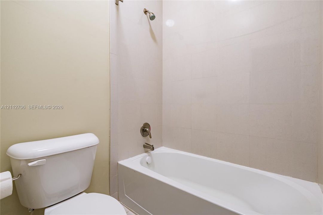 Bathtub with neutral-toned wall tile surround, showerhead, single-lever metal mixing valve, and white porcelain toilet