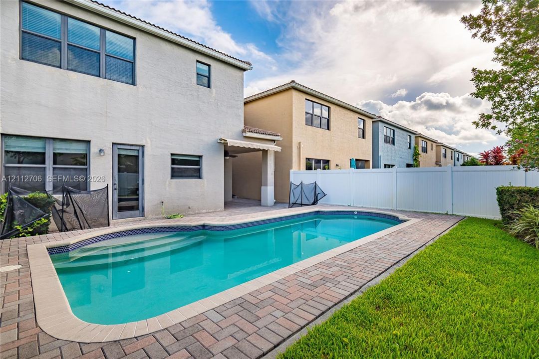 In-ground swimming pool with integrated steps, surrounded by a paved stone patio, covered lanai, and white vinyl privacy fencing