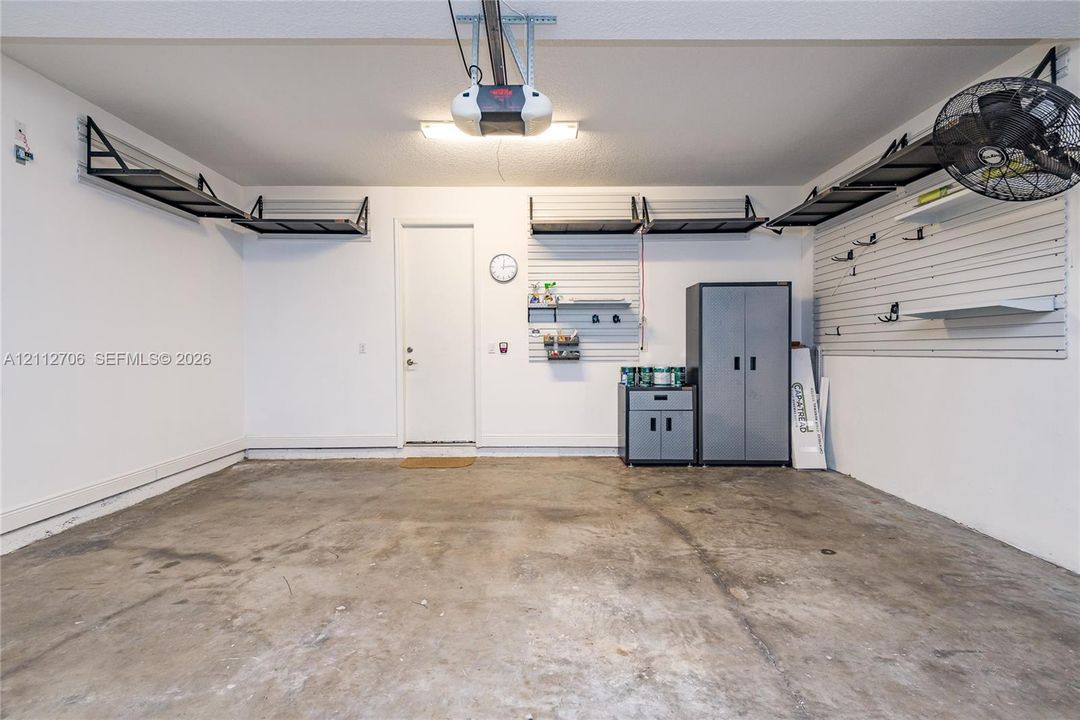 Garage space featuring overhead storage racks, integrated wall-mounted slat organization systems, a concrete floor, and an automated garage door opener