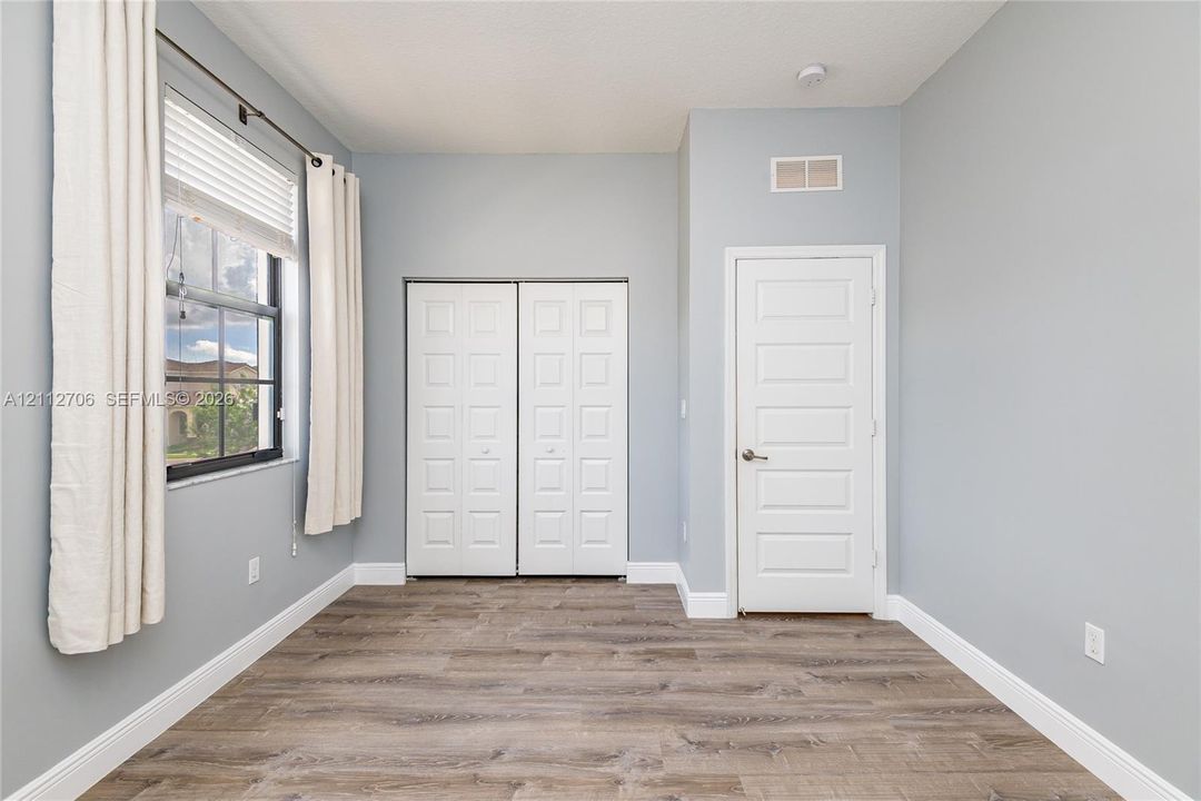 Room featuring wood-finish flooring, a single-hung window with a metal frame, dual-panel closet doors, and a solid-core interior door
