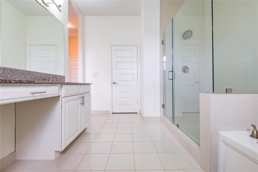 Bathroom featuring white cabinetry, stone-surface countertop, tile flooring, glass-enclosed shower, and a built-in vanity station