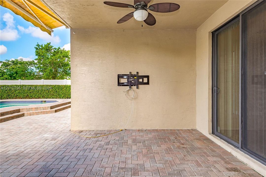 Covered patio featuring brick paver flooring, a ceiling fan, a retractable awning, and a wall-mounted television bracket