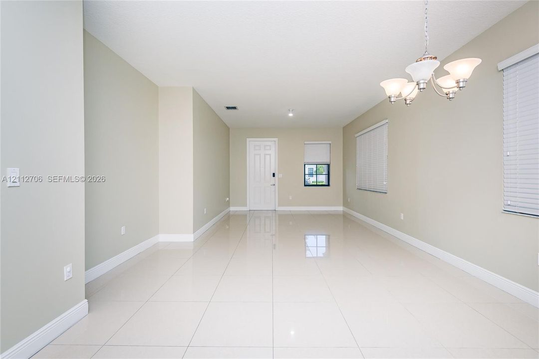 Neutral-toned interior featuring large-format tile flooring, multi-arm chandelier lighting, and windows equipped with horizontal blinds