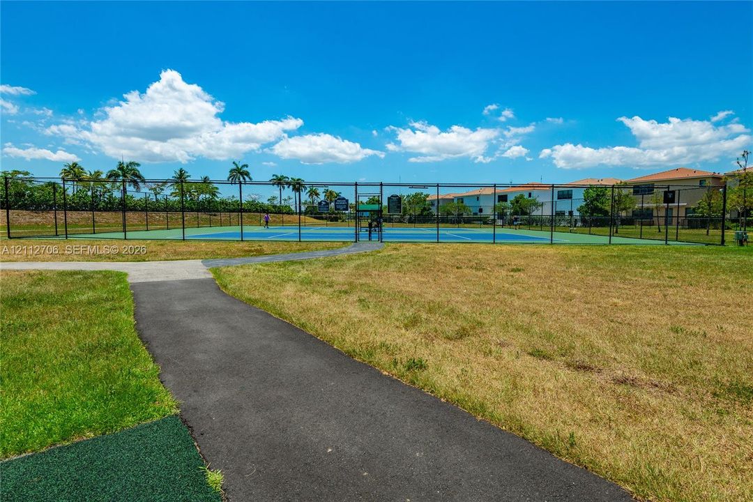 Tennis court with a fenced perimeter, hard surface, and paved asphalt walkway