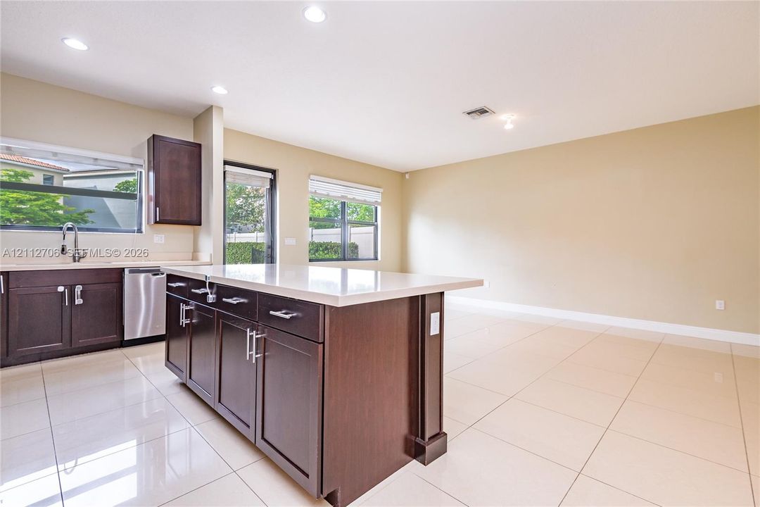 Kitchen featuring dark wood cabinetry, a central island with a solid surface countertop, stainless steel appliances, large-format tile flooring, and recessed lighting