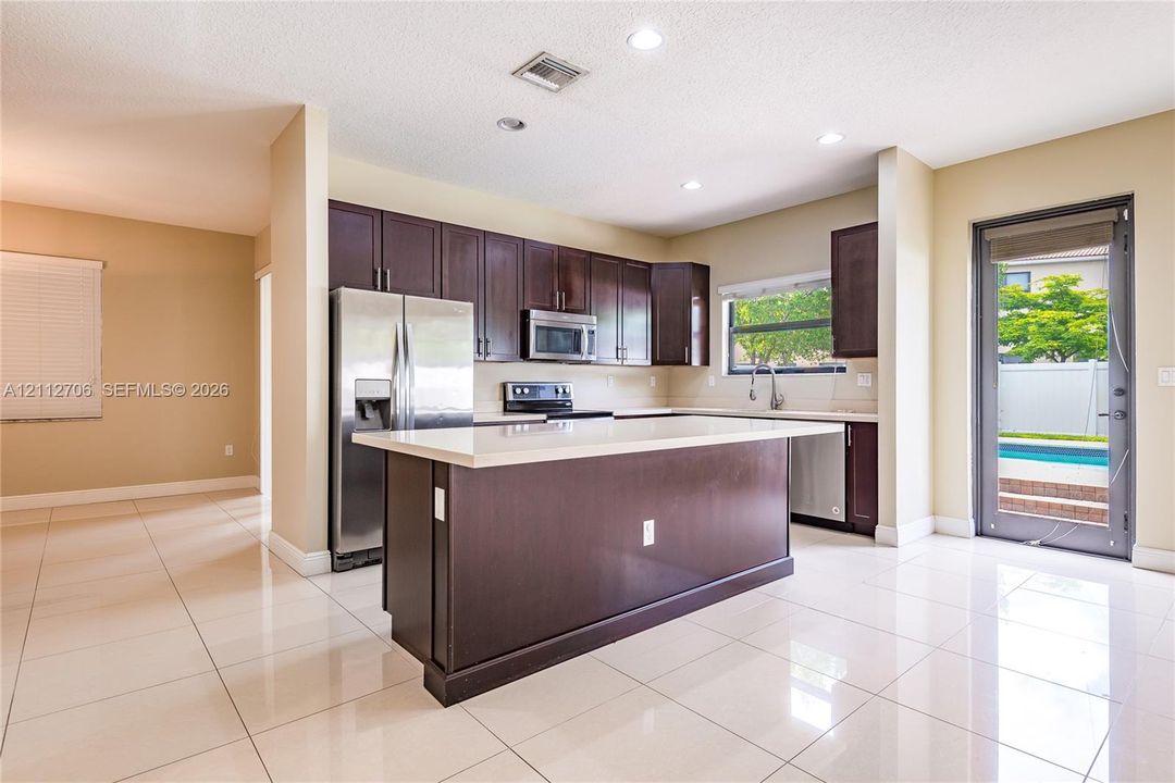 Kitchen featuring espresso-toned cabinetry, stainless steel appliances, central island with quartz countertop, recessed lighting, and large-format tile flooring