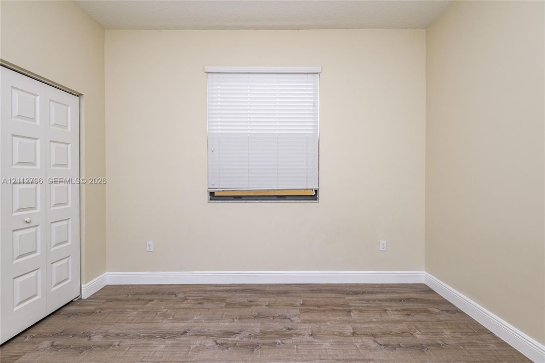Neutral interior space featuring wood-finish flooring, a single window with horizontal blinds, and a built-in closet with paneled double doors