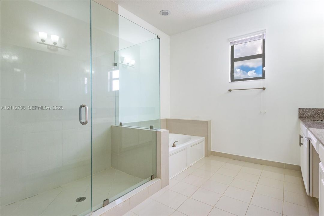 Frameless glass shower enclosure with tile flooring, deep-set soaking tub, neutral-tone tile surround, and vanity with stone countertop