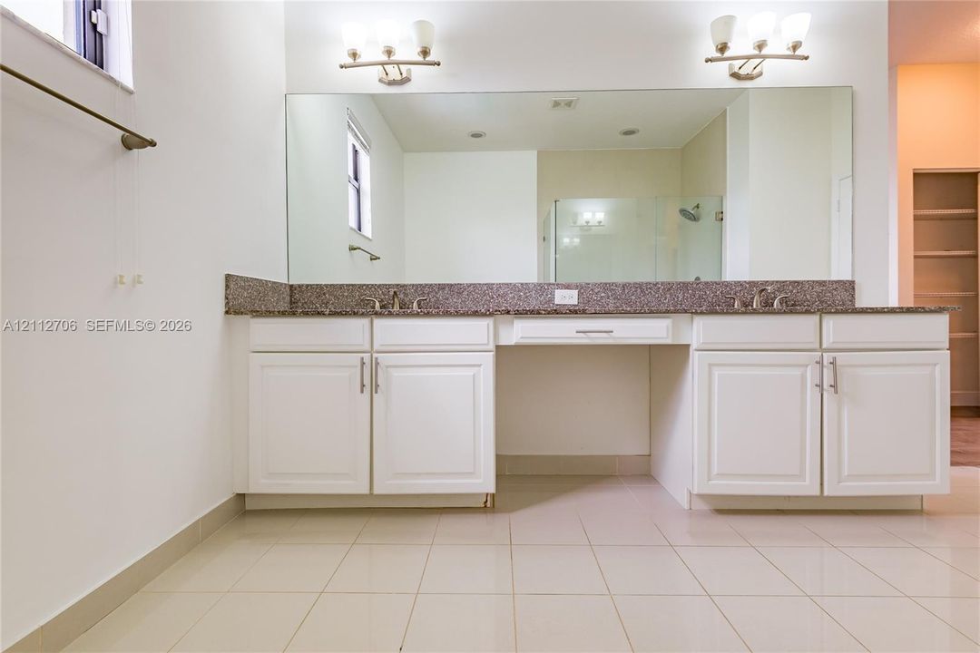 Dual-sink vanity with stone countertop, central seated vanity area, full-width wall mirror, and dual light fixtures