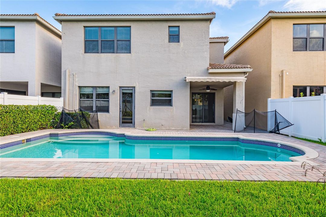 Two-story stucco exterior featuring a private in-ground swimming pool, paver patio, covered lanai with ceiling fan, and privacy fencing