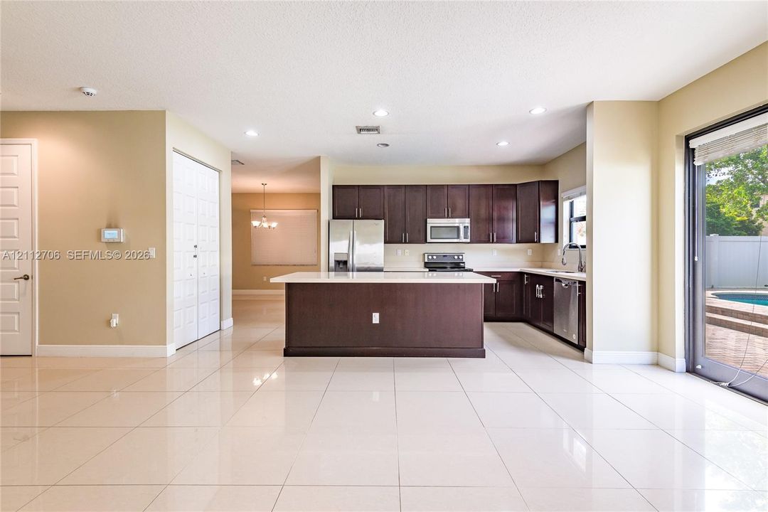Kitchen featuring dark wood cabinetry, a central island with a solid surface countertop, stainless steel appliances, and large-format tile flooring
