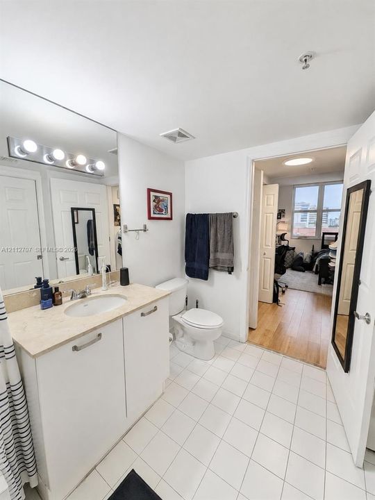 Bathroom featuring white cabinetry, integrated sink with light-toned stone countertop, full-width vanity mirror, and ceramic tile flooring