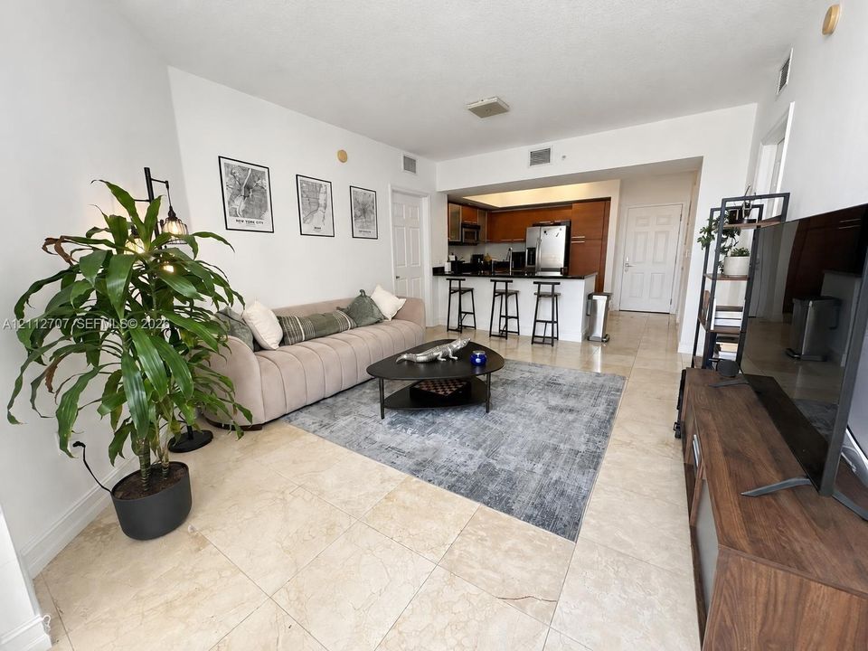 Open-concept interior featuring large-format tile flooring, kitchen with breakfast bar, dark-tone cabinetry, and stainless steel appliances