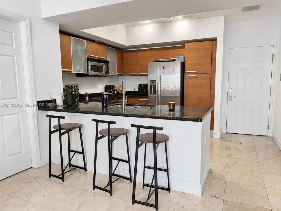 Kitchen featuring wood-finish cabinetry, dark stone-style countertops, stainless steel appliances, and a breakfast bar