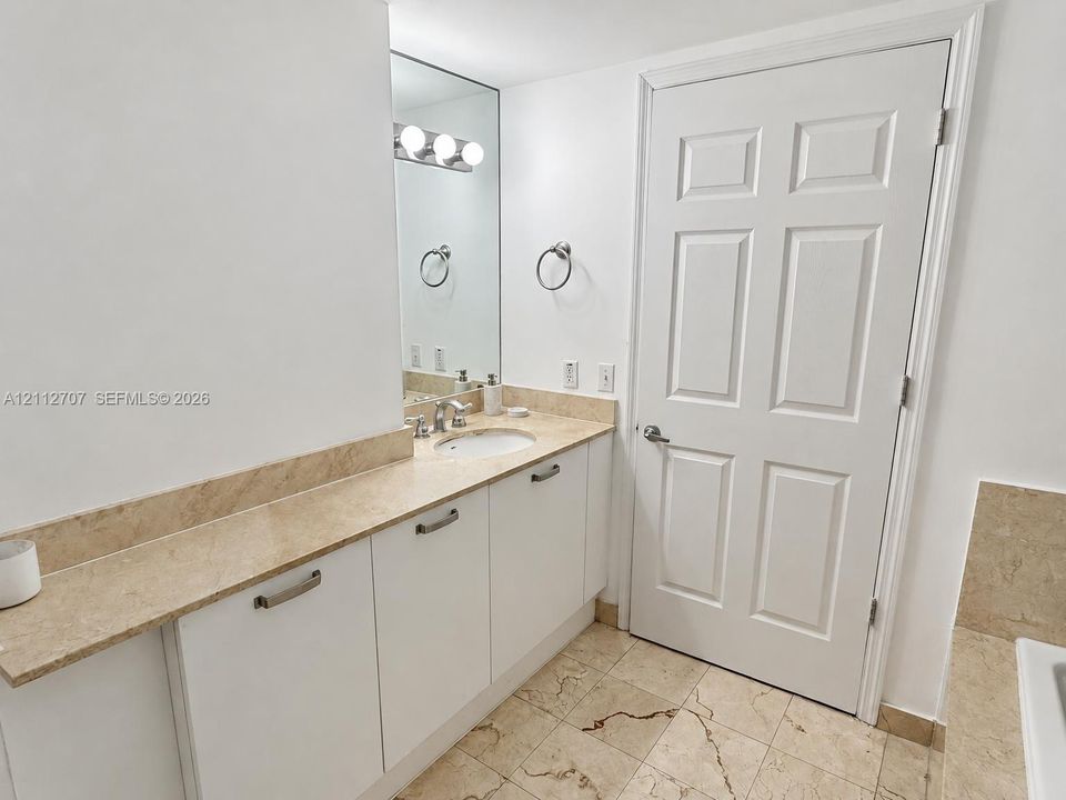 Vanity featuring stone-surfaced countertop, integrated basin, white cabinetry with metallic hardware, and wall-mounted vanity lighting