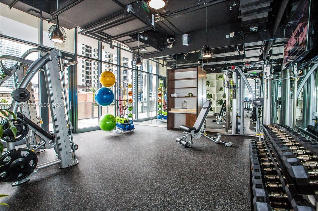 Fitness center featuring floor-to-ceiling glass walls, industrial-style exposed ceiling, rubberized flooring, and built-in shelving
