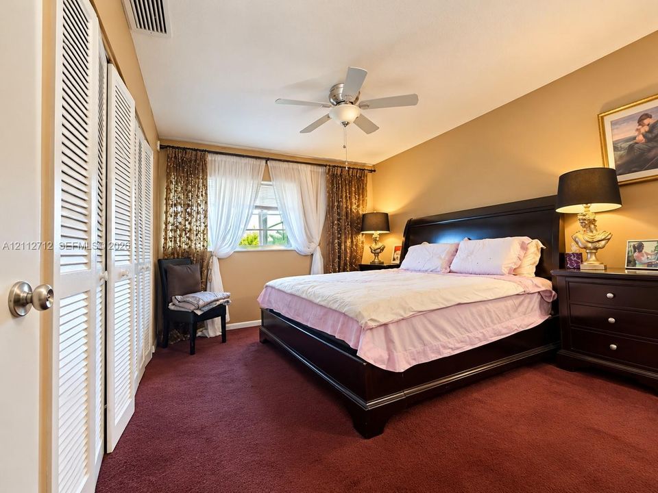 Bedroom featuring plush carpeting, dual louvered-door closets, and a centrally mounted ceiling fan
