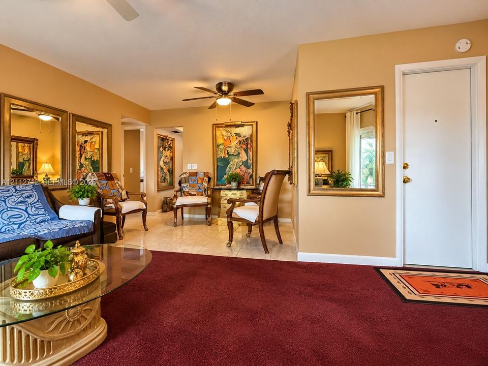Living area featuring wall-to-wall carpeting, polished tile flooring, a ceiling fan with integrated lighting, and inset wall-mounted mirrors