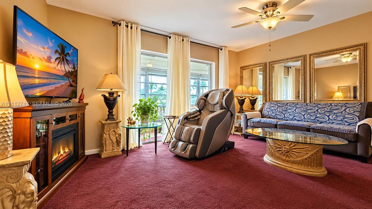 Living area featuring a built-in electric fireplace with a wood-finish media console, wall-to-wall carpeting, a ceiling fan with integrated lighting, and sliding glass doors