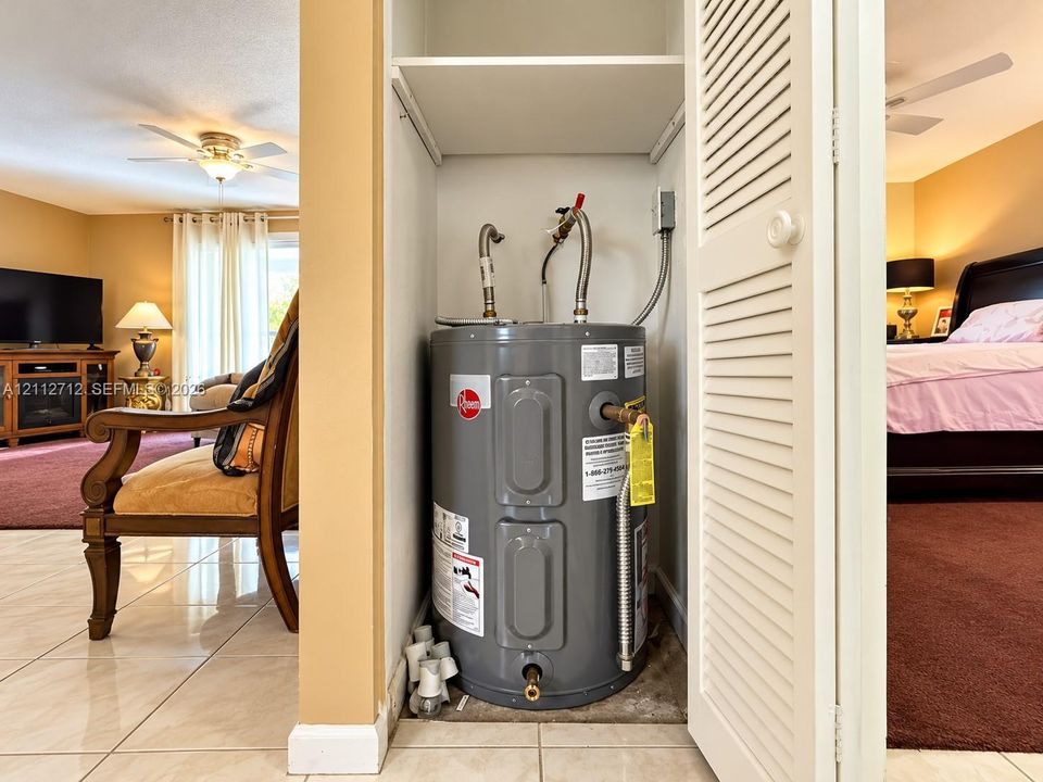 Utility closet featuring a grey Rheem water heater, louvered door, and overhead shelving