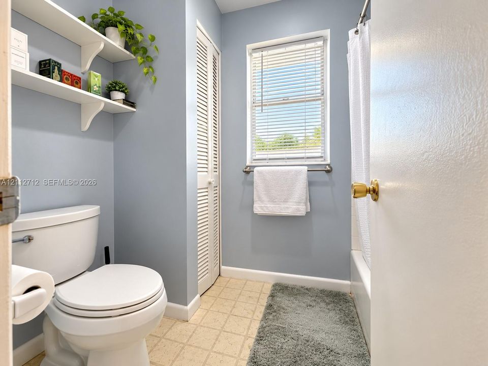 Full bathroom featuring a tub-shower combination, louvered closet doors, wall-mounted shelving, and a window with blinds