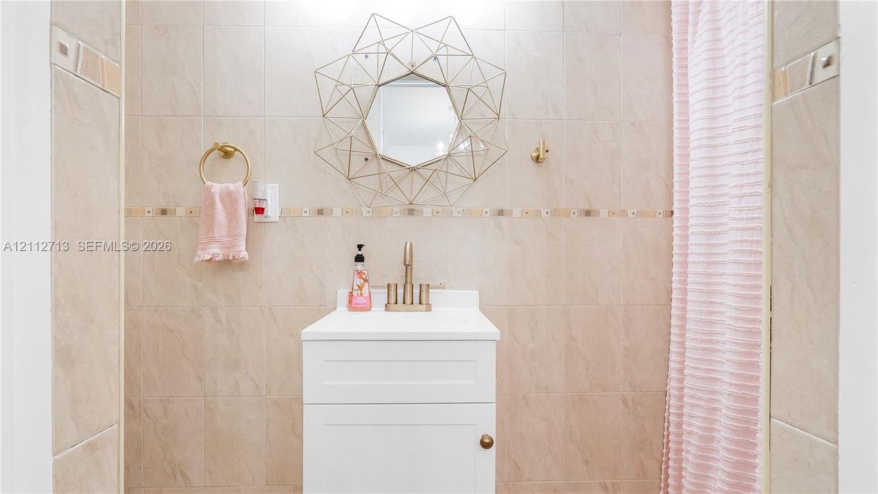 White vanity with a rectangular sink, metallic faucet, wall-mounted circular geometric mirror, and floor-to-ceiling tile featuring a decorative accent border