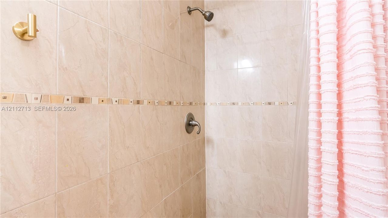 Shower enclosure featuring large-format beige wall tiling, a decorative glass and stone mosaic accent border, and a metallic single-handle pressure-balance valve