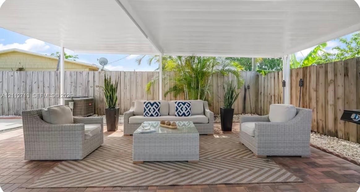 Covered patio featuring a solid-surface overhead structure, concrete paver flooring, and full-height wood-panel privacy fencing