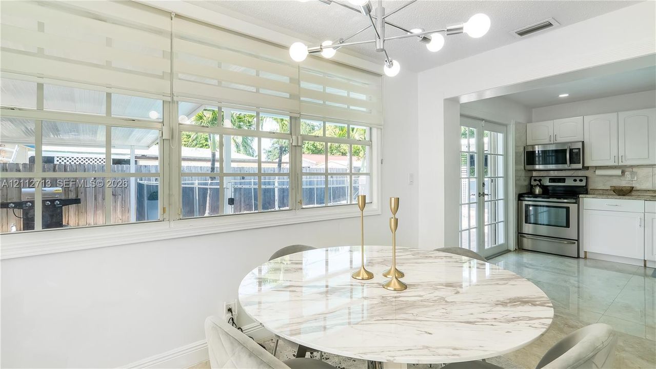 Multi-pane window wall with roller shades, modern multi-arm sputnik chandelier, white cabinetry, stainless steel appliances, and tile flooring
