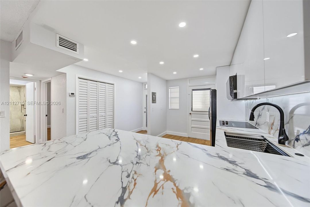 Kitchen featuring high-gloss cabinetry, stone-patterned waterfall countertop, recessed lighting, integrated appliances, and matte black arched faucet