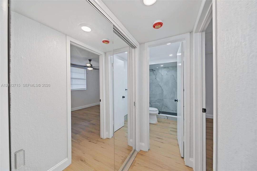 Hallway featuring mirrored sliding closet doors, wood-finish flooring, and recessed ceiling lighting