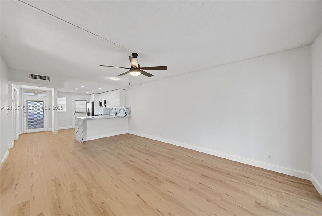 Open-concept interior featuring light wood-finish flooring, a ceiling fan with integrated lighting, recessed ceiling illumination, and kitchen peninsula with waterfall-edge stone-look surfacing