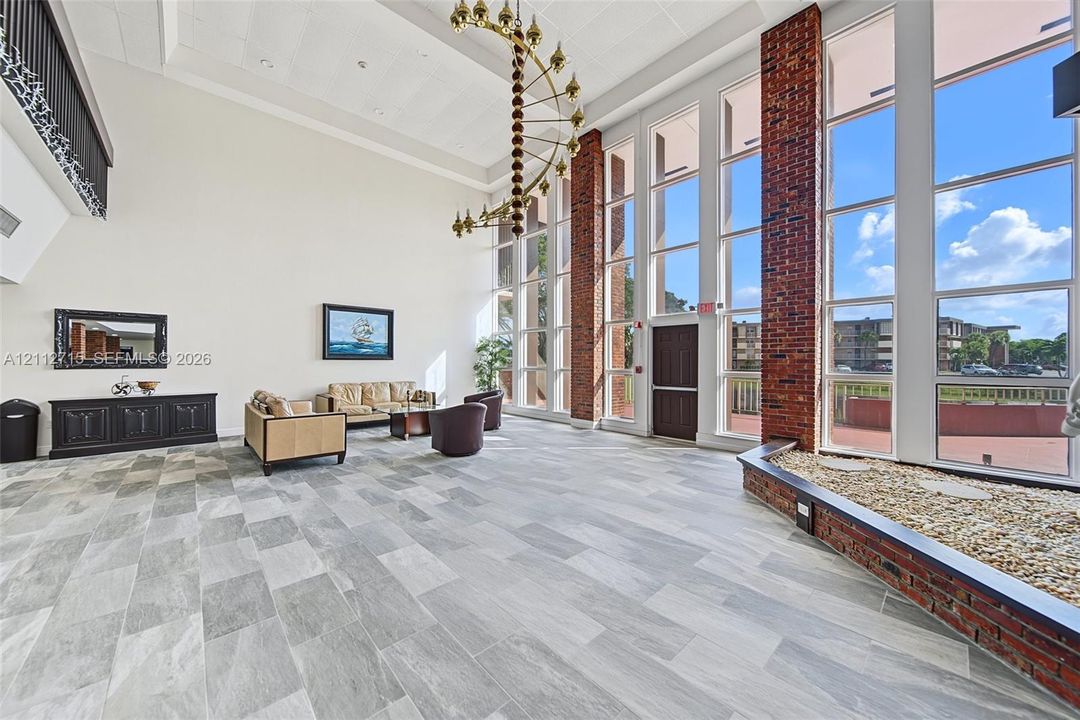 Vaulted ceiling featuring a multi-tiered chandelier, full-height windows, exposed brick columns, stone-tile flooring, and an integrated interior brick planter